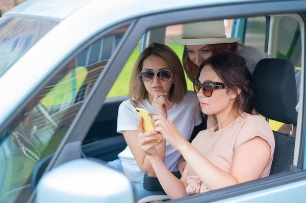 Três namoradas felizes fazem uma viagem. Mulheres estão dirigindo em um carro e tirando uma selfie em um telefone celular — Fotografia de Stock
