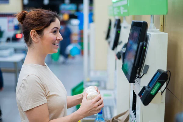 Caucasian woman uses a self-checkout counter. Self-purchase of groceries in the supermarket without a seller
