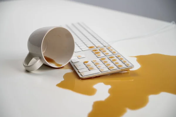 Xícara derramada de café preto no teclado do computador na mesa branca. — Fotografia de Stock