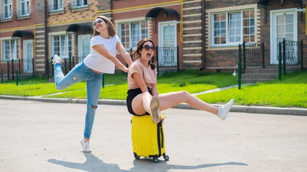 Tre gioiosi amici caucasici si divertono e si rincorrono mentre cavalcano una valigia. Le donne eccitate vanno in viaggio. La bionda bruna e la rossa vanno in vacanza. — Foto Stock
