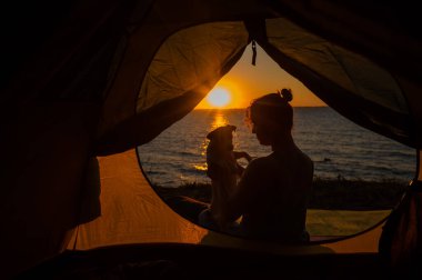 Gün doğumunda bir kadın ve bir köpek turist çadırında. Evcil bir hayvanla kamp yapmak.
