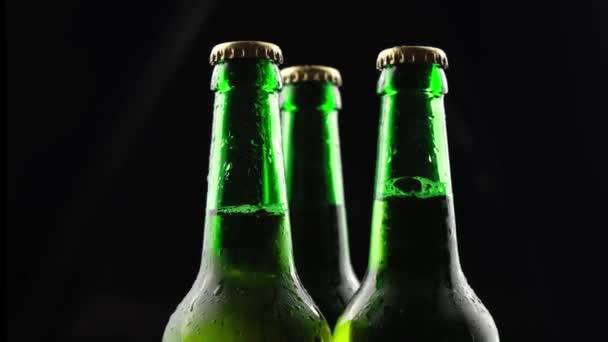 Três garrafas de cerveja de vidro verde girando em um fundo preto no escuro — Vídeo de Stock