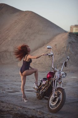 Yüksek topuklu seksi iç çamaşırlı kızıl saçlı kadın motosiklette oturuyor. Çekici kızıl saçlı kız gün batımında motosiklette oturuyor.