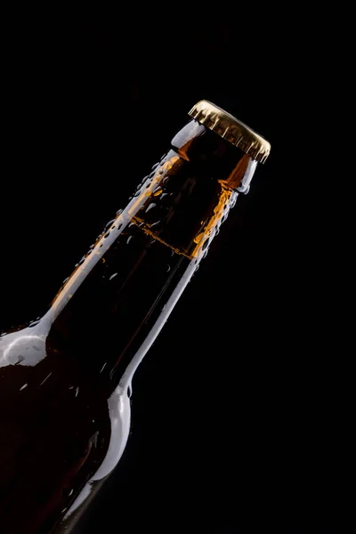 Dark glass beer bottle with condensation drops on black background.