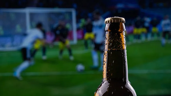 A bottle of beer on the background of a broadcast of a football match.