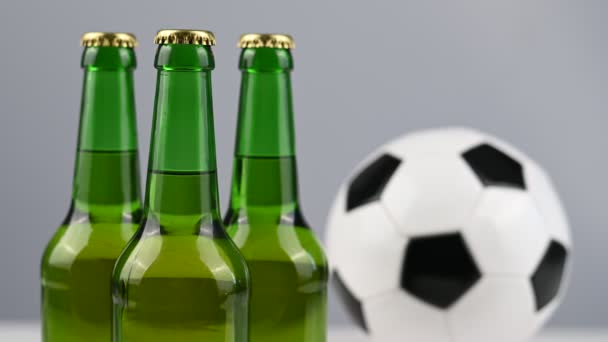 Un pallone da calcio sta girando accanto a tre bottiglie di birra su uno sfondo bianco — Video Stock