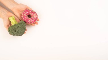 Yeme alışkanlıkları karşılaştırması. Beyaz arka planda brokoli ve çörek tutan bir kadın. Boşluğu kopyala