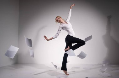 Takım elbiseli zarif bir balerin stüdyoya doküman atıyor. İş kadını beyaz arka planda yalınayak dans ediyor.