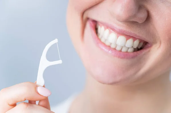 Close-up portret van een mooie blanke vrouw met een vlekkeloze glimlach met een tandenstoker met tandzijde op een witte achtergrond — Stockfoto