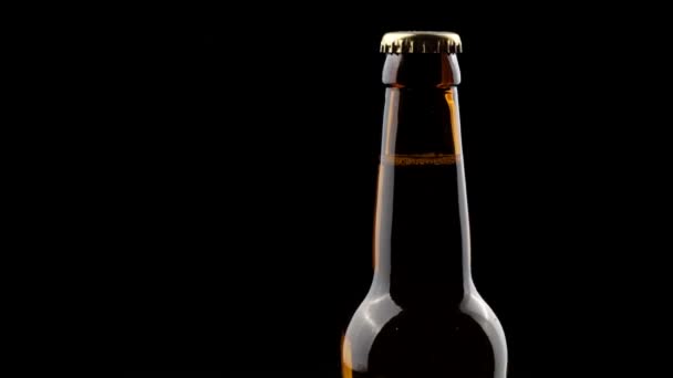 Botella de vidrio de cerveza girando en la oscuridad sobre un fondo negro — Vídeo de stock