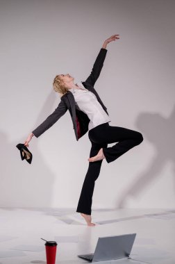 Beyaz bir arka planda ayakkabıları ile atlayan takım elbiseli zarif çıplak ayaklı bir balerin..