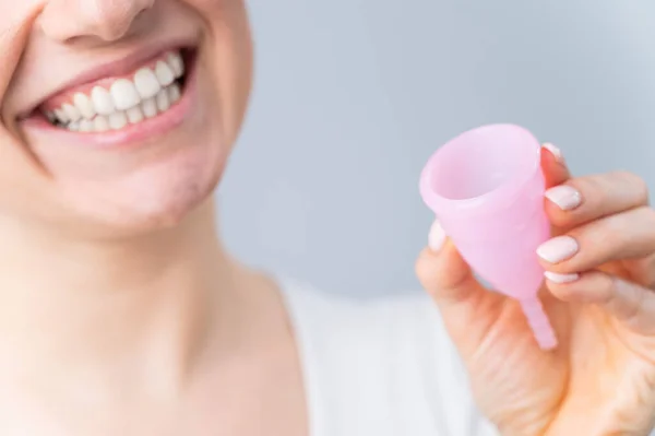 Close-up retrato de mulher branca sorridente segurando copo menstrual rosa no fundo branco. Alternativa para tampões e almofadas em dias críticos. — Fotografia de Stock