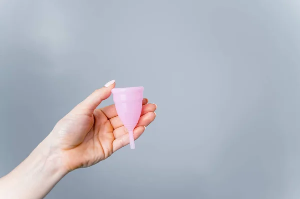 Close-up of a female hand with a pink menstrual cup on a white background. Caring for the environment. Eco friendly female intimate hygiene product. Copy space — 图库照片