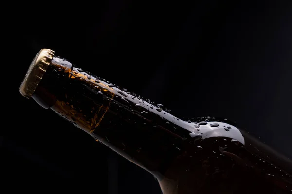 Темная стеклянная бутылка пива с капельками конденсата на черном фоне. — стоковое фото