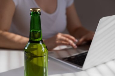 Beyaz kadın dizüstü bilgisayarda çalışıyor ve cam şişeden bira içiyor.