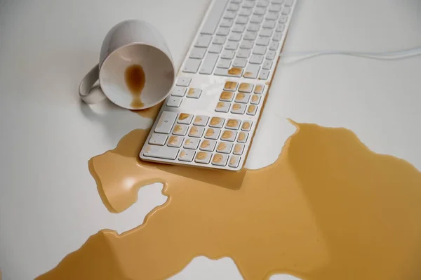 Rozlitý šálek černé kávy na klávesnici počítače na bílém stole. — Stock fotografie
