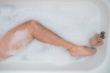 Rahatlatıcı bir banyo yapan bir adamın komik bir fotoğrafı. Köpük banyosunda erkek ayağının yakın çekimi. Üst görünüm