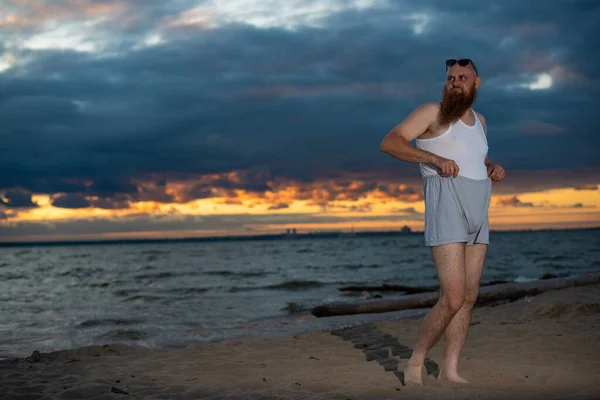 Un uomo calvo brutale posa sulla spiaggia al tramonto parodia pulcino glamour — Foto Stock