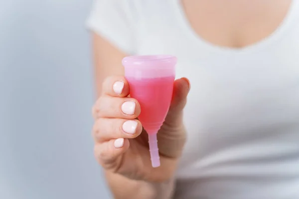 Una donna senza volto che indossa una t-shirt bianca tiene una tazza mestruale rosa con liquido rosso all'interno — Foto Stock