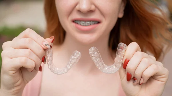 Krásná mladá rusovlasá žena s rovnátky na zubech drží odnímatelné podpěry venku — Stock fotografie