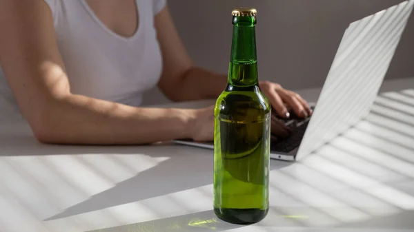 Femme blanche travaille à un ordinateur portable et boit de la bière à partir d'une bouteille en verre — Photo