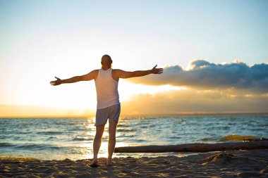 Gün batımında sahilde tişörtlü ve boksörlü acımasız bir adamın komik bir portresi.