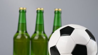 Bir futbol topu beyaz arka planda üç şişe biranın yanında dönüyor.