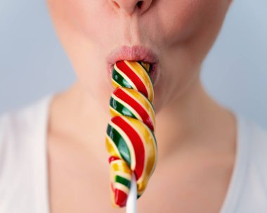Close-up portrait of a woman sucking a long lollipop against a white background. Blowjob simulation