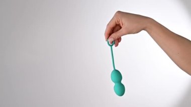 Yüzü olmayan kadın turkuaz bir vajina topu gösteriyor. Beyaz arka planda pelvik zemin kaslarını çalıştırmak için kegel antrenörü tutan bir kız..