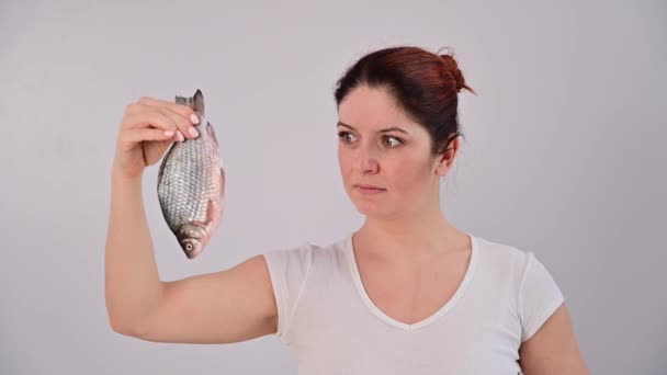 白人女性は魚の匂いに怯え、白い背景に服ピンで鼻をつまむ。. — ストック動画