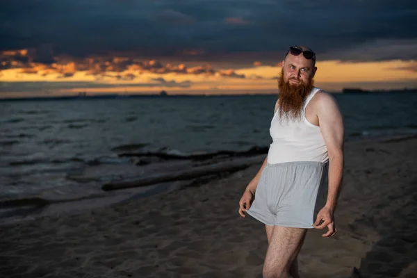 Жестокий лысый мужчина позирует на пляже на закате пародийная гламурная цыпочка — стоковое фото