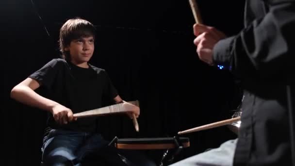 Νεαρή λευκή γυναίκα διδάσκει σε ένα αγόρι να παίζει ντραμς στο στούντιο σε μαύρο φόντο. Μαθητής μουσικής σχολής — Αρχείο Βίντεο