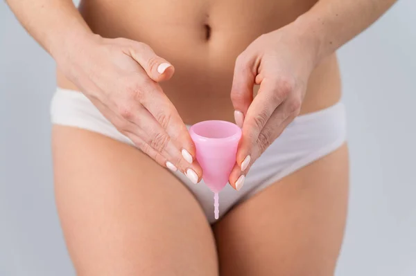 Close-up of a woman in white cotton panties holding a pink menstrual cup against a white background. Alternative to tampons and pads — Stock Photo, Image