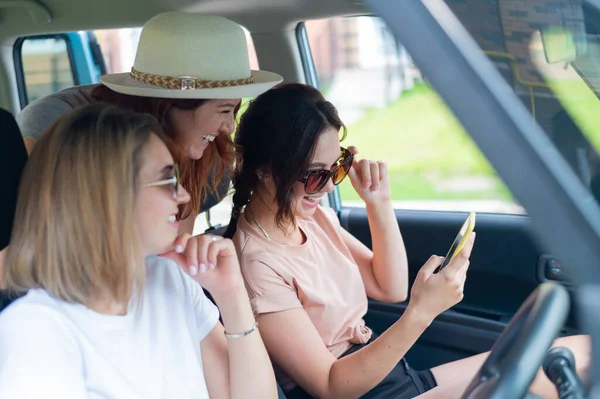 Três namoradas felizes fazem uma viagem. Mulheres estão dirigindo em um carro e tirando uma selfie em um telefone celular — Fotografia de Stock