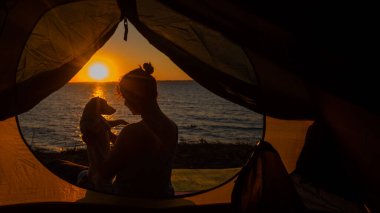 Gün doğumunda bir kadın ve bir köpek turist çadırında. Evcil bir hayvanla kamp yapmak.