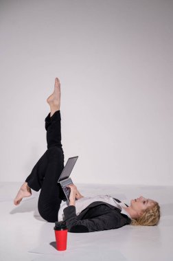 İş elbisesi giymiş çıplak ayaklı balerin dizüstü bilgisayara poz veriyor ve kahve içiyor. Bilgisayar başında esnek bir kadın çalışıyor.