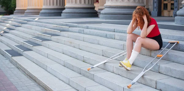 Девушка с травмой ноги сидит на лестнице с костылями. — стоковое фото
