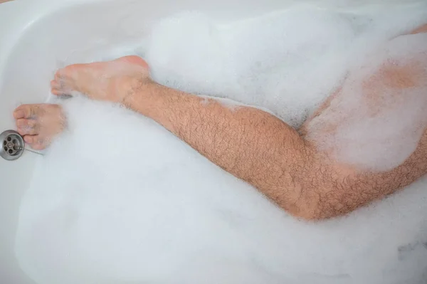 한 남자가 쉬는 목욕을 하고 있는 이상 한 사진입니다. 거품 목욕을 하고 있는 남성 발의 근접 사진. 위에서 본 풍경 — 스톡 사진