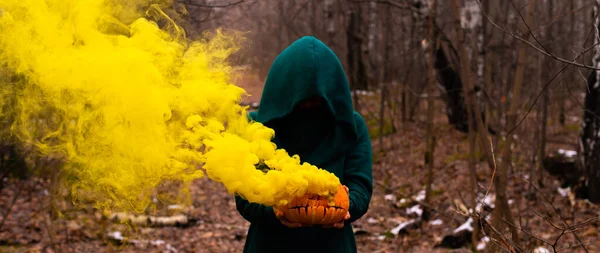 Una bruja espeluznante sostiene una calabaza humeante en un bosque profundo. Jack o lantern emite humo amarillo para Halloween — Foto de Stock