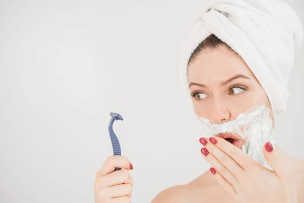 Wesoła biała kobieta z ręcznikiem na głowie i pianką do golenia na twarzy trzyma brzytwę na białym tle — Zdjęcie stockowe