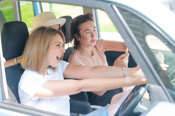 Três amigos vão numa viagem. Mulheres caucasianas dirigem em um carro e apontam os dedos de surpresa. — Fotografia de Stock