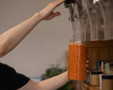 Bir adam kavanoza kırmızı mercimek dolduruyor. Bir eco mağazasında ağırlıkla mal satmak. Plastik ambalajsız ticaret kavramı