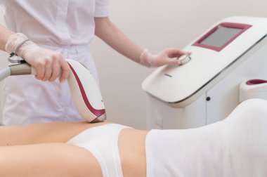 Profesyonel güzellik salonundaki bir kadın, lazer tüyü çıkararak bikini bölgesindeki istenmeyen bitkileri temizliyor.