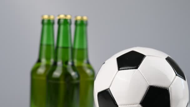 En fotboll snurrar bredvid tre flaskor öl på en vit bakgrund — Stockvideo