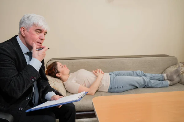 Λευκή γυναίκα ξαπλώνει στον καναπέ σε μια δεξίωση με έναν ψυχοθεραπευτή. Ένας ηλικιωμένος δουλεύει ως ψυχίατρος. — Φωτογραφία Αρχείου