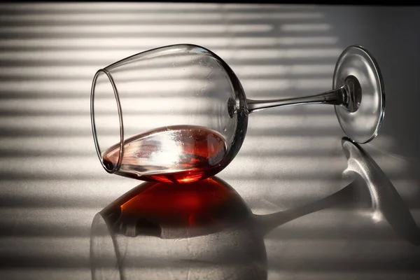 A glass of red wine lies on its side on a white table with a shade from the blinds — Stock Photo, Image