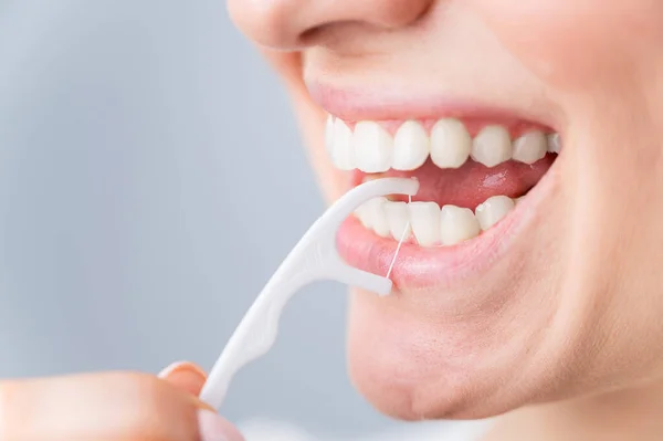 Blanke vrouw poetsen tanden met tandenstoker met tandzijde op witte achtergrond. — Stockfoto
