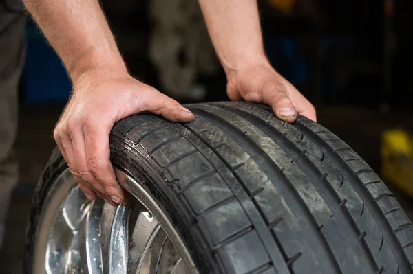 Um mecânico de automóveis segura uma roda de um carro. Mudança de pneus de carro de acordo com a temporada — Fotografia de Stock