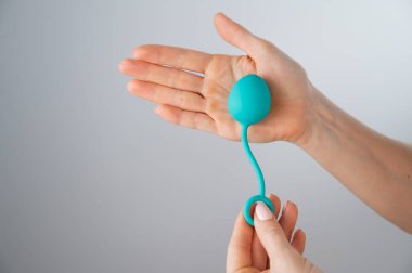 Yüzü olmayan bir kadın nane renginde bir vajina topu gösteriyor. Beyaz arka planda pelvik zemin kaslarını çalıştırmak için kegel antrenörü tutan bir kız..