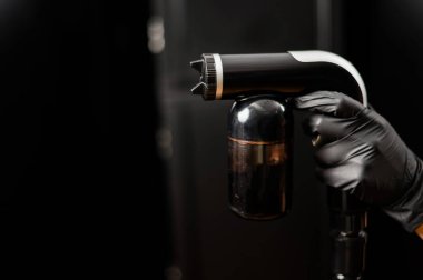 Bir ustanın ellerinde hazır bronzlaşma ekipmanlarının yakın çekimi. Siyah arka plana karşı deri boya sıkmak.